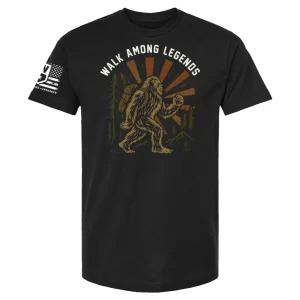 Black unisex t-shirt with Walk Among Legends Bigfoot hiker graphic, pine trees, sunburst, and arched text “Walk Among Legends”